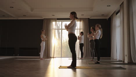 In-slow-motion-a-yoga-instructor-conducts-a-group-lesson-for-women-of-different-ages-and-weight-categories-thin-and-full-in-the-gym-in-the-morning-in-the-sun.-The-glare-of-the-sun-on-the-floor
